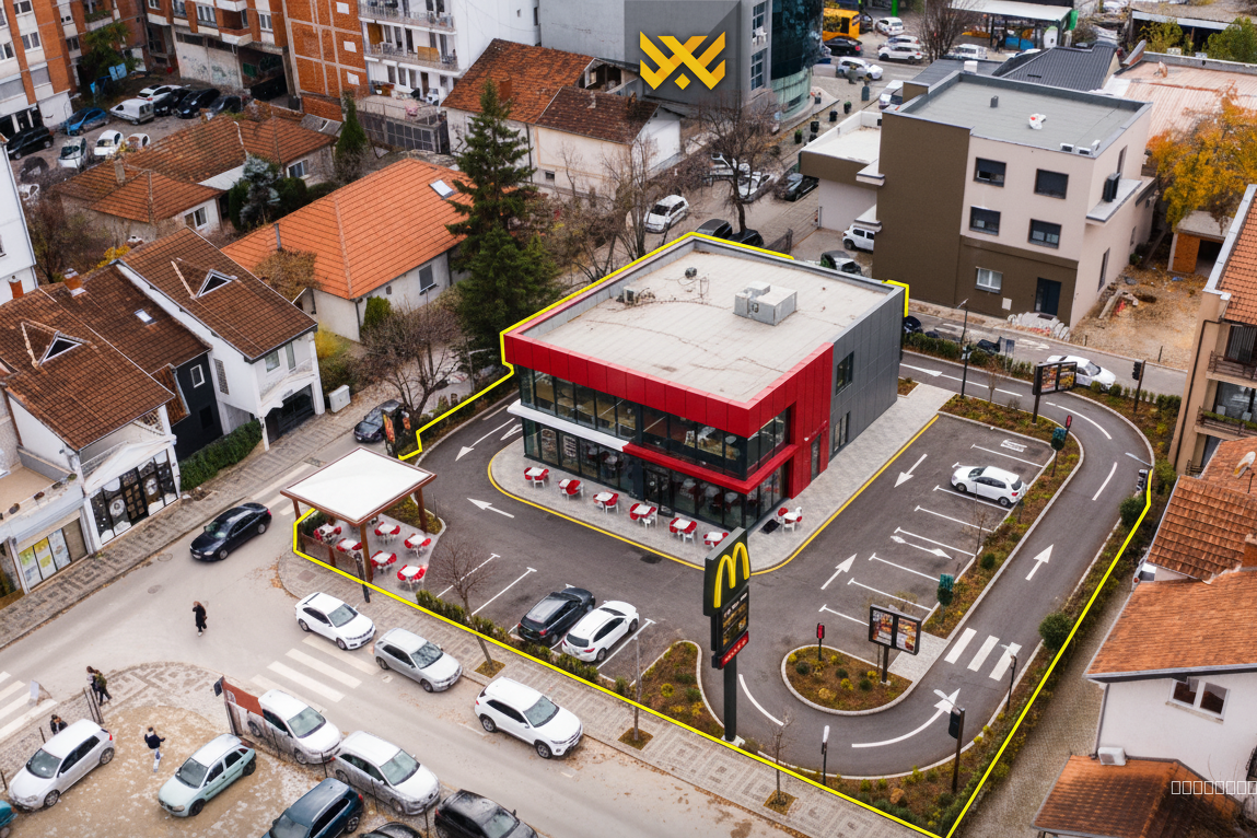 Project Context:
The selected building in the uploaded photos (marked 550m² + 150m²) is located in a dense urban area with strong commercial potential. It is surrounded by residential houses, mid-rise buildings, and high-rise commercial towers nearby. The property sits on a corner-like position with two direct street accesses and high pedestrian and vehicle visibility. There is significant traffic circulation and parking space around the perimeter.

Main Objective:
Transform the existing house and auxiliary structure within the highlighted yellow boundaries into a modern drive-thru restaurant concept, visually similar to well-known food chain brands such as KFC, McDonald’s, or Burger King, while preserving the strategic strengths of the location.

Transformation Requirements:

1. Building Conversion:

Replace the residential house with a contemporary fast-food restaurant building, featuring a clean, modern façade.

Optional: Keep some reference to the existing massing, or completely redesign the volume depending on what gives the best commercial presence.

Add branded architectural elements such as bold signage, illuminated logos, menu boards, canopy structures, and clear material palettes (metal panels, glass, concrete, red/black/white tones depending on style).

Integrate large glass windows on the front façade for visibility and a welcoming street presence.

2. Drive-Thru System:

Design a functional drive-thru lane that wraps around the building, using the available space shown in the images.

Include ordering station, digital menu boards, speaker box, payment window, and pick-up window.

Ensure the lane is smooth, intuitive, and uses the natural flow of the property.

Visualize clear directional arrows and drive-thru signage.

3. Parking & Access Points:

Highlight the excellent access from both connecting streets shown in the images.

Create dedicated parking spots for dine-in customers in front and around the building.

Show easy vehicle entry and exit routes.

Maintain or improve the pedestrian sidewalks for customer walk-in flow.

4. Branding & Atmosphere:

The final render should resemble a recognizable fast-food chain design (you may choose between KFC, McDonald’s, Burger King style or create a neutral all-purpose drive-thru look).

Add outdoor seating if appropriate.

Modern lighting, landscaping, and clean pavement are required to present an attractive commercial destination.

5. Location & Visibility:

Emphasize the property’s exceptional location by showing how the restaurant stands out within the neighborhood.

Capture visibility from the main roads, pedestrian areas, and the surrounding commercial district with high-rise buildings in the background.

Show how the transformation increases commercial presence and turns the property into a high-traffic business point.

Deliverables Requested:

Exterior architectural renders from multiple angles (street level + aerial).

A clear visualization of the drive-thru lane function.

A realistic representation of how the property would look as a fully operational fast-food chain.

Show day-time lighting, busy but clean atmosphere, and a polished, investor-ready concept.

Image References Provided:

Use the uploaded aerial and top-down photos as reference for exact building boundaries, lot lines, circulation patterns, and context.